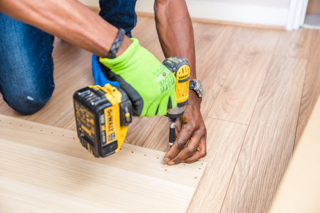 Services Close-up of handyman drilling wood indoors with green gloves and cordless drill.