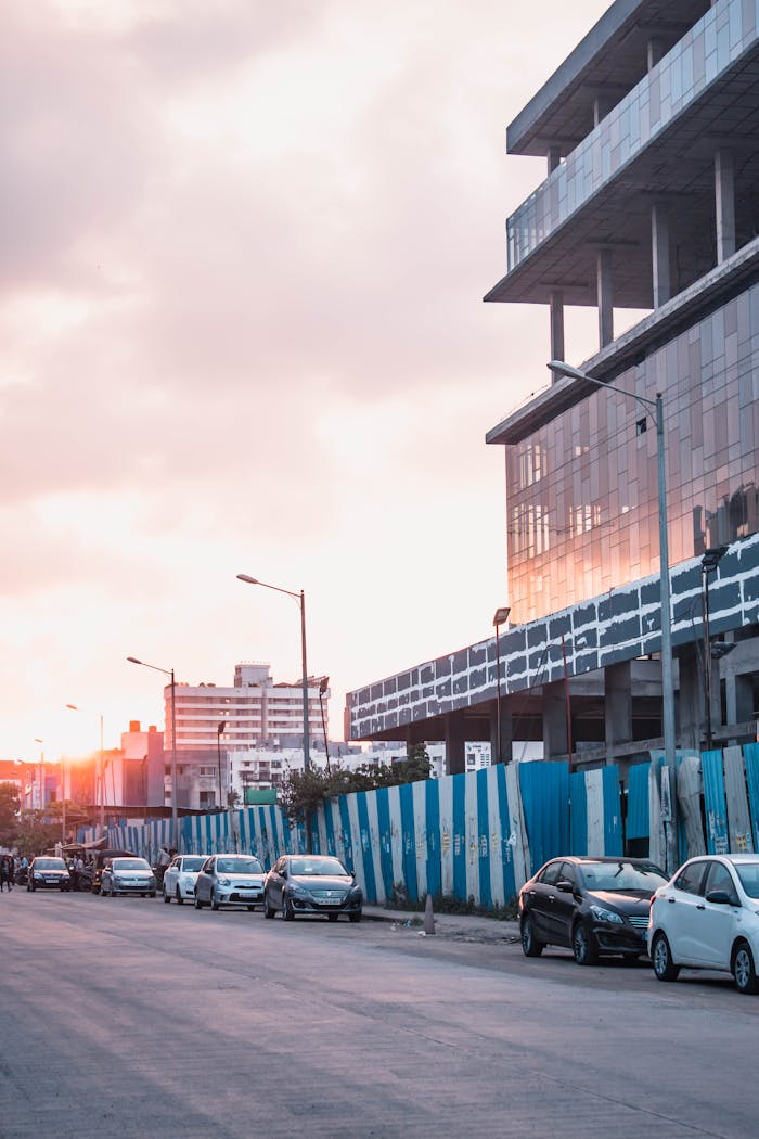 Vibrant street view of under-construction buildings in Pune, India during sunset with parked cars.